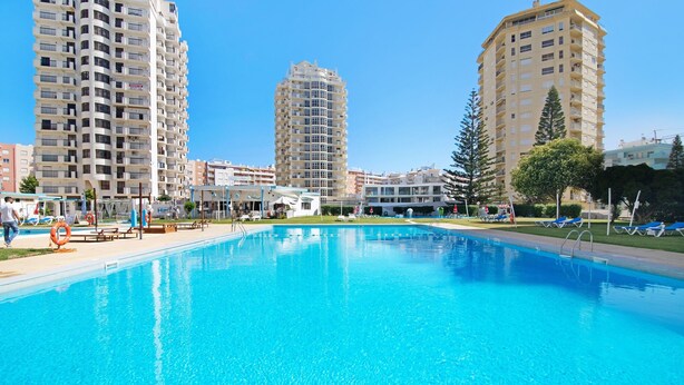 A swimming pool with lounge chairs and a lifebuoy, surrounded by tall residential buildings.