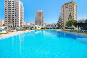 A swimming pool with lounge chairs and a lifebuoy, surrounded by tall residential buildings.