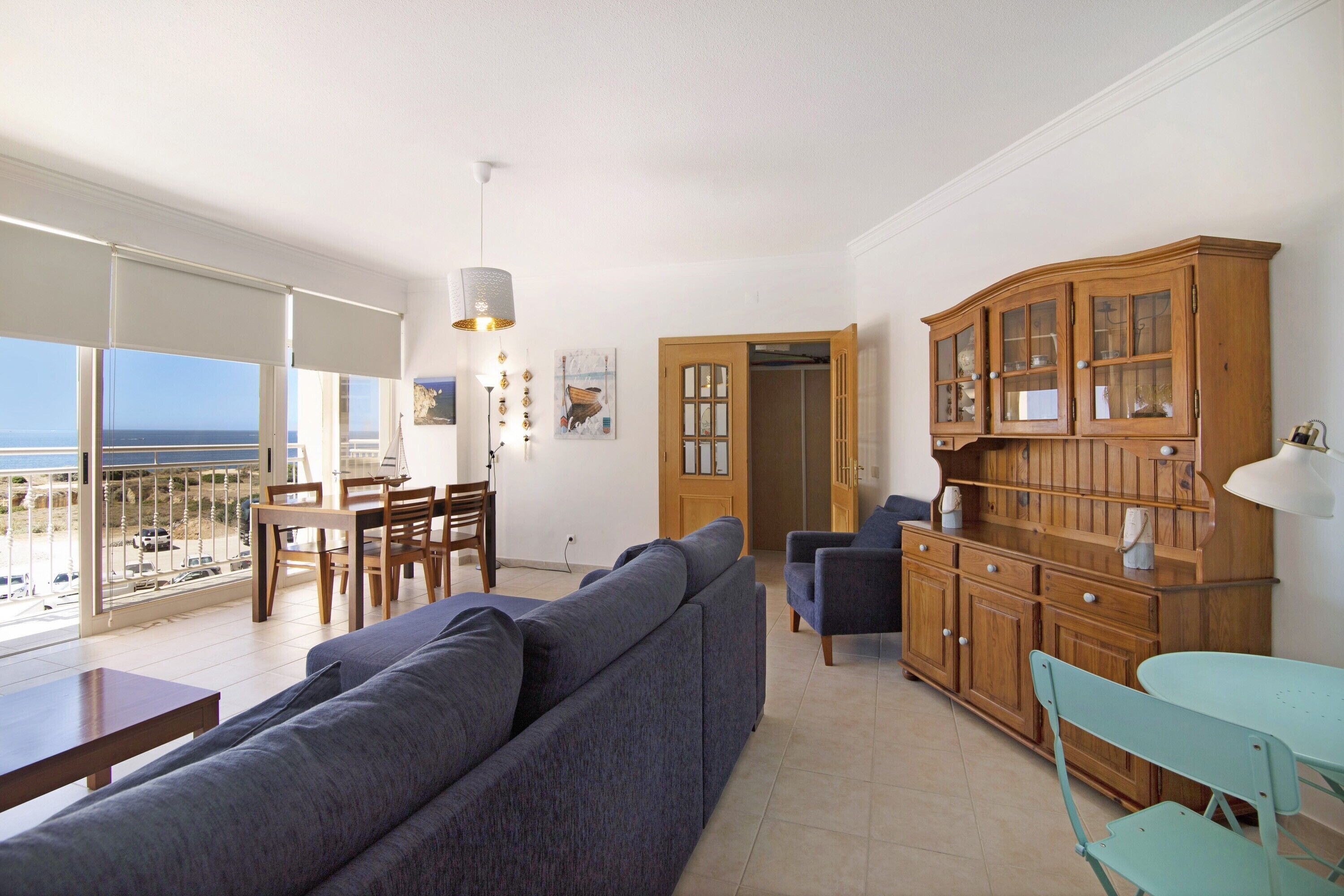 Ein Wohnzimmer mit Sofa, Esstisch, Stühlen, einem Schrank und Blick aufs Meer.