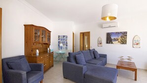 A living room with two sofas, a wooden cabinet, a small table, and a wall-mounted air conditioner.