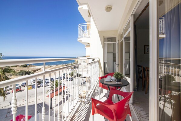 Un balcon avec vue sur la mer, une table avec des chaises et une plante en pot.