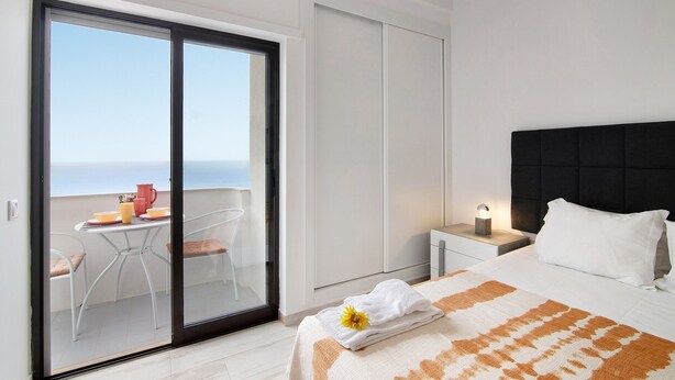 A bedroom with a bed, a nightstand, a bedside table, a window with a view, and a balcony with a table and chairs. - Apt. Torre Sol 10th 6 - Sea View, A/C and Pool (Armação de Pêra)