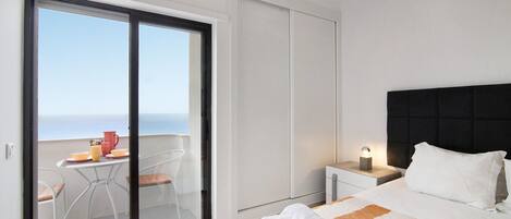 Een slaapkamer met een bed, nachtkastje, raam met uitzicht en balkon met een tafel en stoelen.