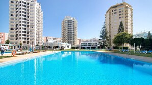 A swimming pool with lounge chairs, surrounded by tall residential buildings. - Apt. Torre Sol 10th 6 - Sea View, A/C and Pool (Armação de Pêra)