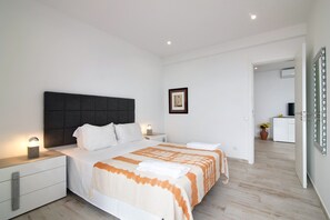Une chambre moderne avec un grand lit, des tables de chevet, un tableau encadré au mur et une vue sur la pièce adjacente.