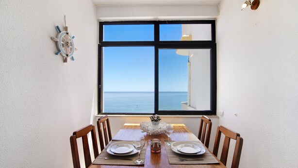 Une table à manger avec des chaises, une vue sur la mer par la fenêtre et une décoration murale représentant un gouvernail de navire.