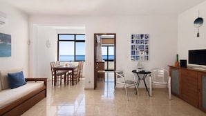 Un salon comprenant un canapé, une table à manger, des chaises, un téléviseur et une vue sur la mer.