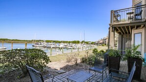 Un patio con mobiliario exterior, vistas a un puerto deportivo con barcos y un edificio con balcón.