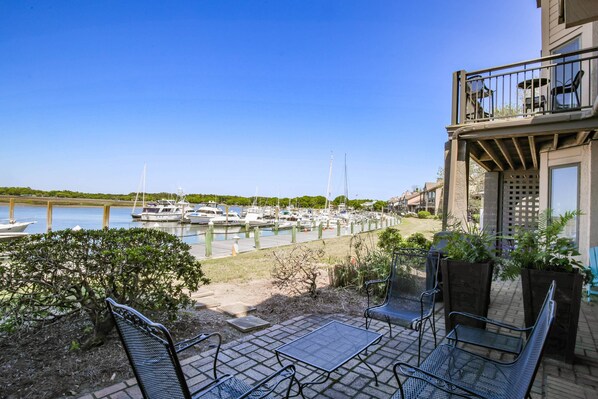 Un patio con mobiliario exterior, vistas a un puerto deportivo con barcos y un edificio con balcón.