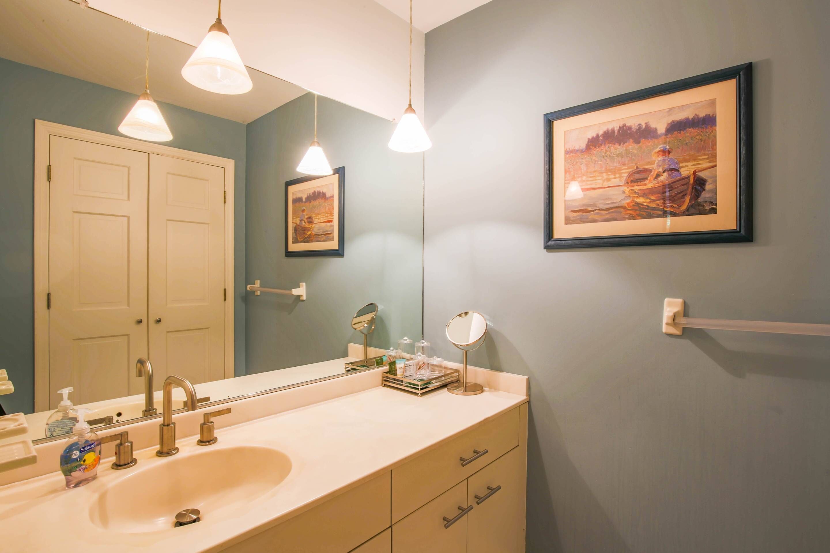Un bagno con lavandino, specchio e due quadri appesi al muro.