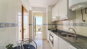 A kitchen with white cabinets, a granite countertop, a stainless steel sink, and a view through an open door. - Oura 11th Floor Beach Apartment with Sea View, Pool, A/C, Wi-Fi, Garden & Balcony (Armação de Pêra)