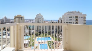 A balcony with a view of a swimming pool, adjacent buildings, and the sea. - Oura 11th Floor Beach Apartment with Sea View, Pool, A/C, Wi-Fi, Garden & Balcony (Armação de Pêra)
