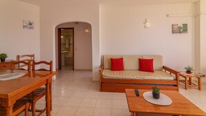 A room with a dining table, a sofa, a small table with a plant, and a doorway leading to another room. - Oura 11th Floor Beach Apartment with Sea View, Pool, A/C, Wi-Fi, Garden & Balcony (Armação de Pêra)