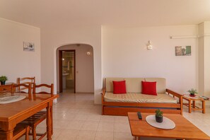 A room with a dining table, a sofa, a small table with a plant, and a doorway leading to another room.