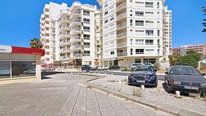 Un edificio residencial de varios pisos con balcones, un área pavimentada y automóviles estacionados.