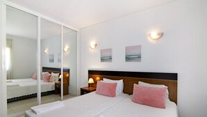 Habitación de hotel con una cama grande, una mesita de noche con lámpara, un espejo en la pared y una obra de arte colgada.