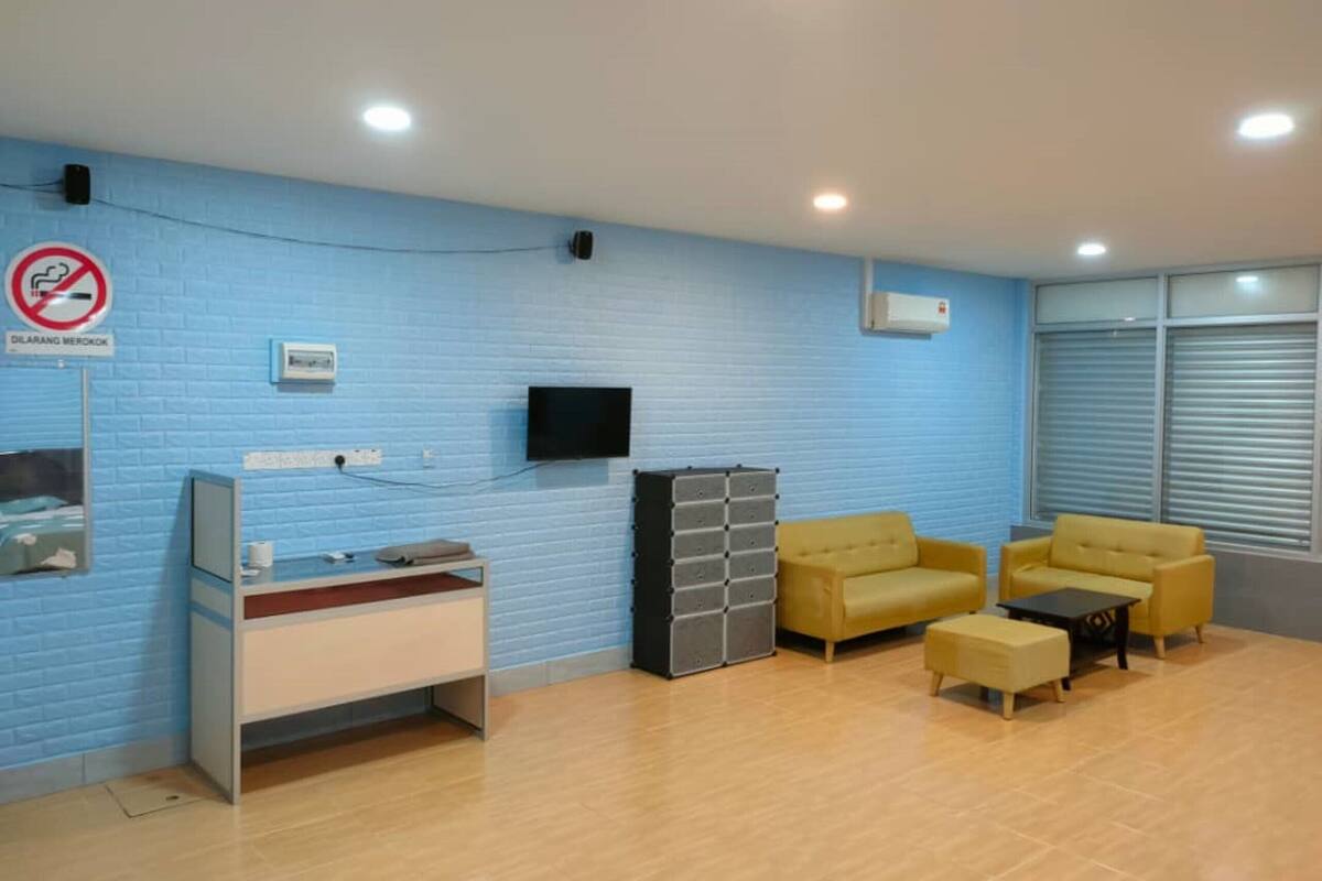 Een receptie met een blauwe bakstenen muur, een flatscreen televisie aan de wand, een bureau met een computer en telefoon, twee gele banken en een kleine tafel.