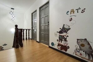 A hallway with wooden flooring, a staircase with a balustrade, and a wall with a cat-themed mural. - OYO 90275 Meow Homestay (Saratok)