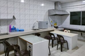 A modern kitchen with white tiles, a built-in stove, a sink, and a dining area with chairs. - OYO 90275 Meow Homestay (Saratok)