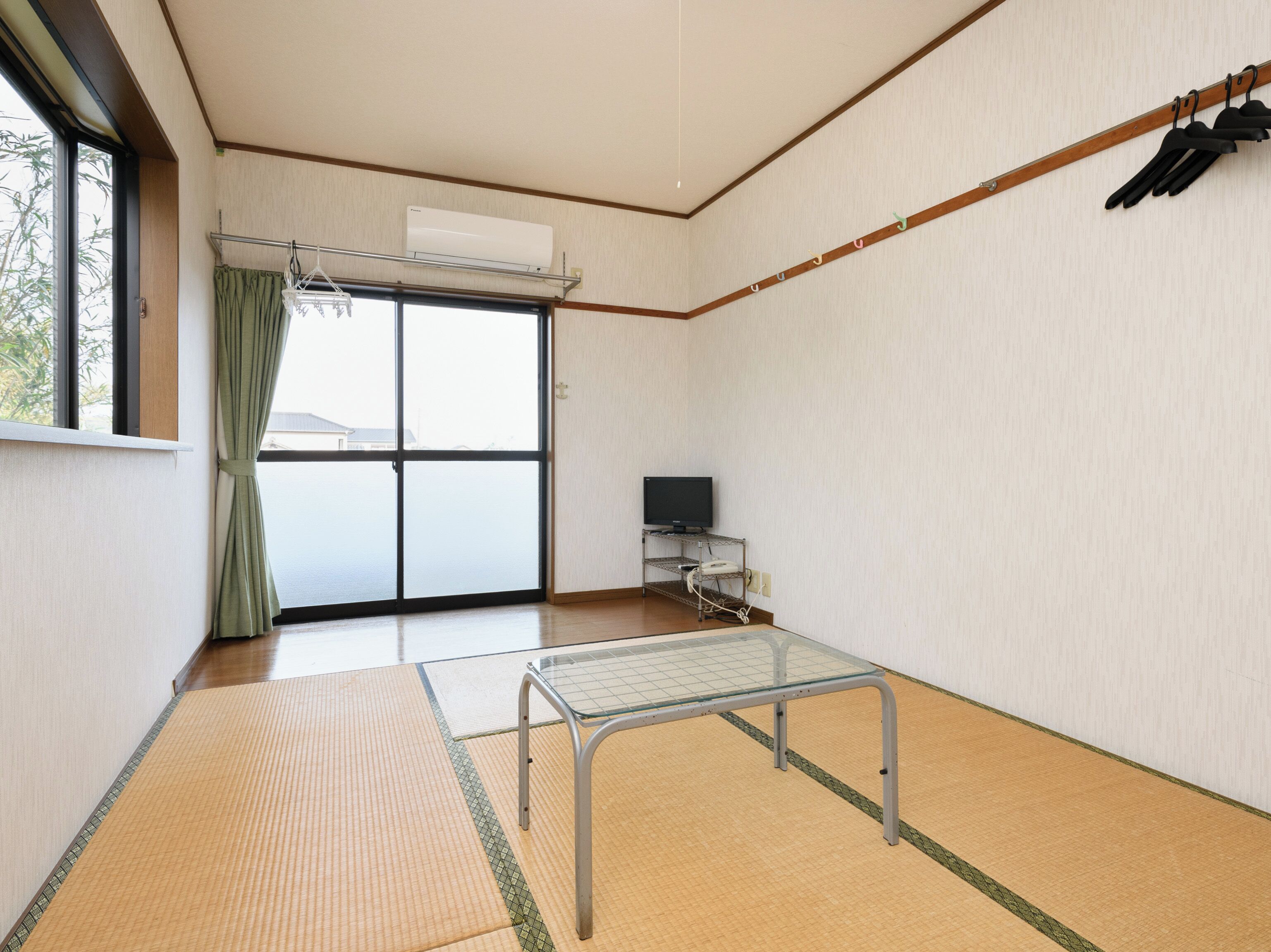 Une pièce avec un sol recouvert de tatamis, un futon servant de lit, un téléviseur posé sur un meuble et une porte coulissante donnant sur l’extérieur.