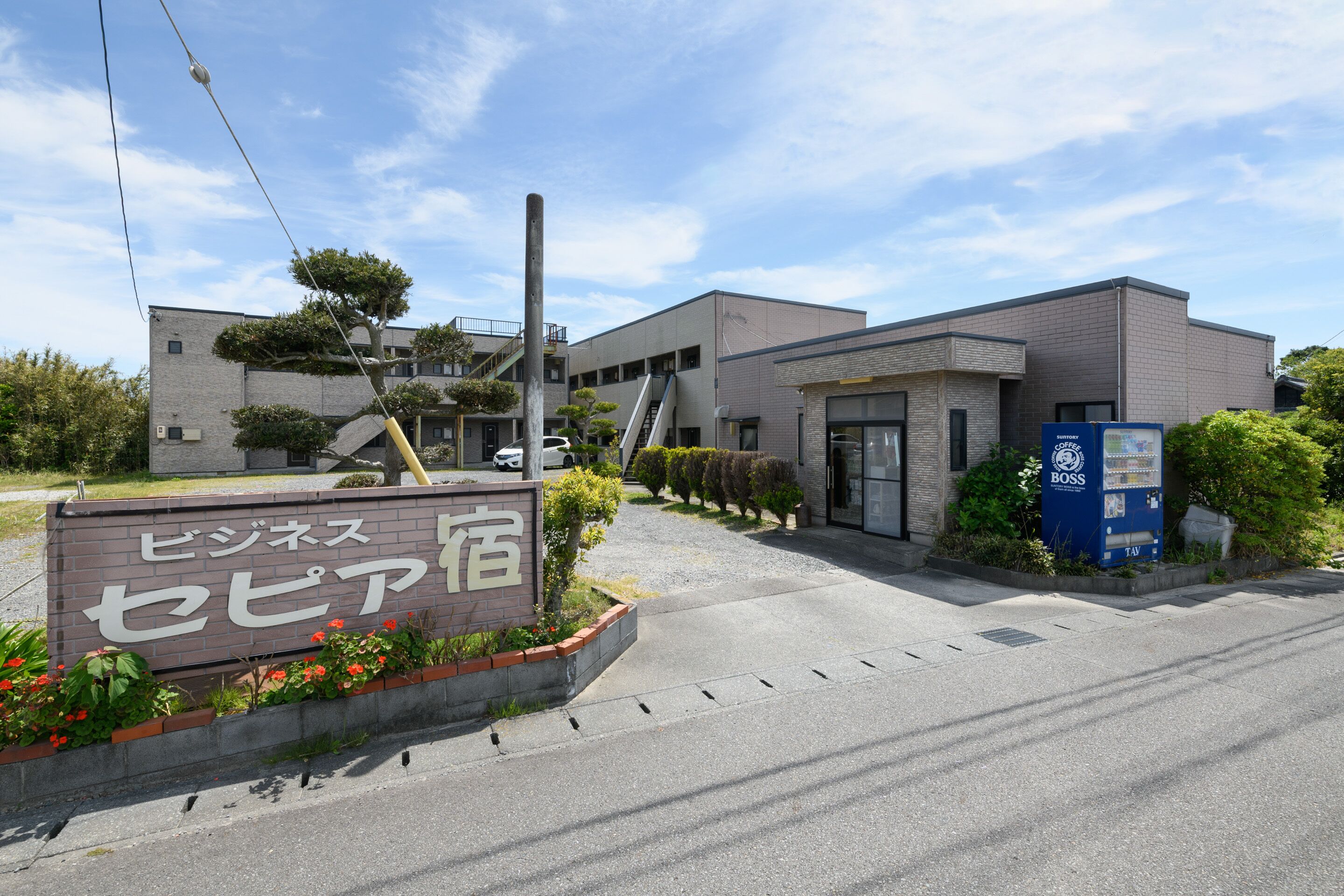 A modern building with a sign in Japanese, a parking area, and a blue vending machine.
