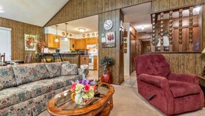 Ein gemütliches Wohnzimmer mit einer Couch, einem roten Sessel und einem Holztisch mit einer floralen Dekoration.