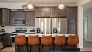 Una cocina moderna con electrodomésticos de acero inoxidable, una isla central con taburetes de bar e iluminación colgante.