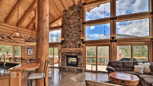 A spacious log cabin interior with a stone fireplace, large windows, and a cozy seating area. - Spacious, Luxe Cabin w/ Mtn Views, Sauna & More! (Villa Grove)