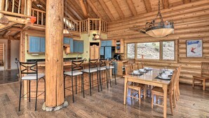 A rustic log cabin interior with a dining area, kitchen, and a loft bedroom. - Spacious, Luxe Cabin w/ Mtn Views, Sauna & More! (Villa Grove)