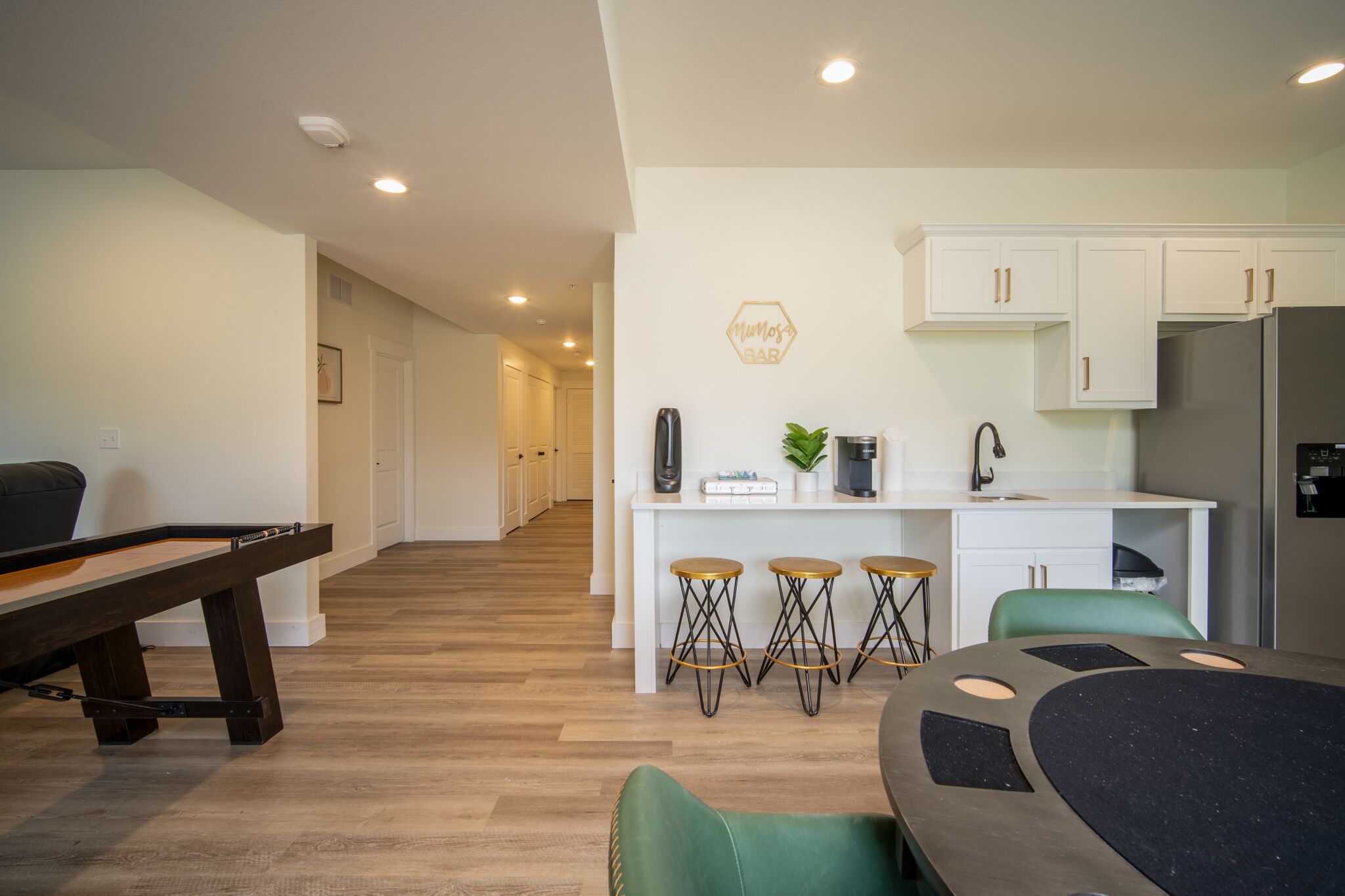 A modern kitchen with white cabinets, a refrigerator, and a bar area with stools.