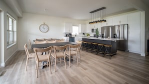 Et moderne køkken med spiseplads, der indeholder en stor ø med barstole, hvide skabe, rustfrie stålemmer og en hængende lampe.