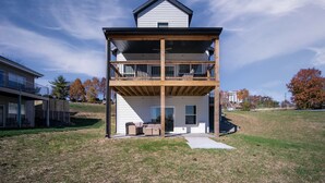 A two-story building with a balcony on the upper floor, a covered outdoor seating area, and a grassy yard. - Gorgeous Reunion Lodge with 2 Decks + Patio, Resrot Amenities, Ticket & Golf Deals! (Branson)