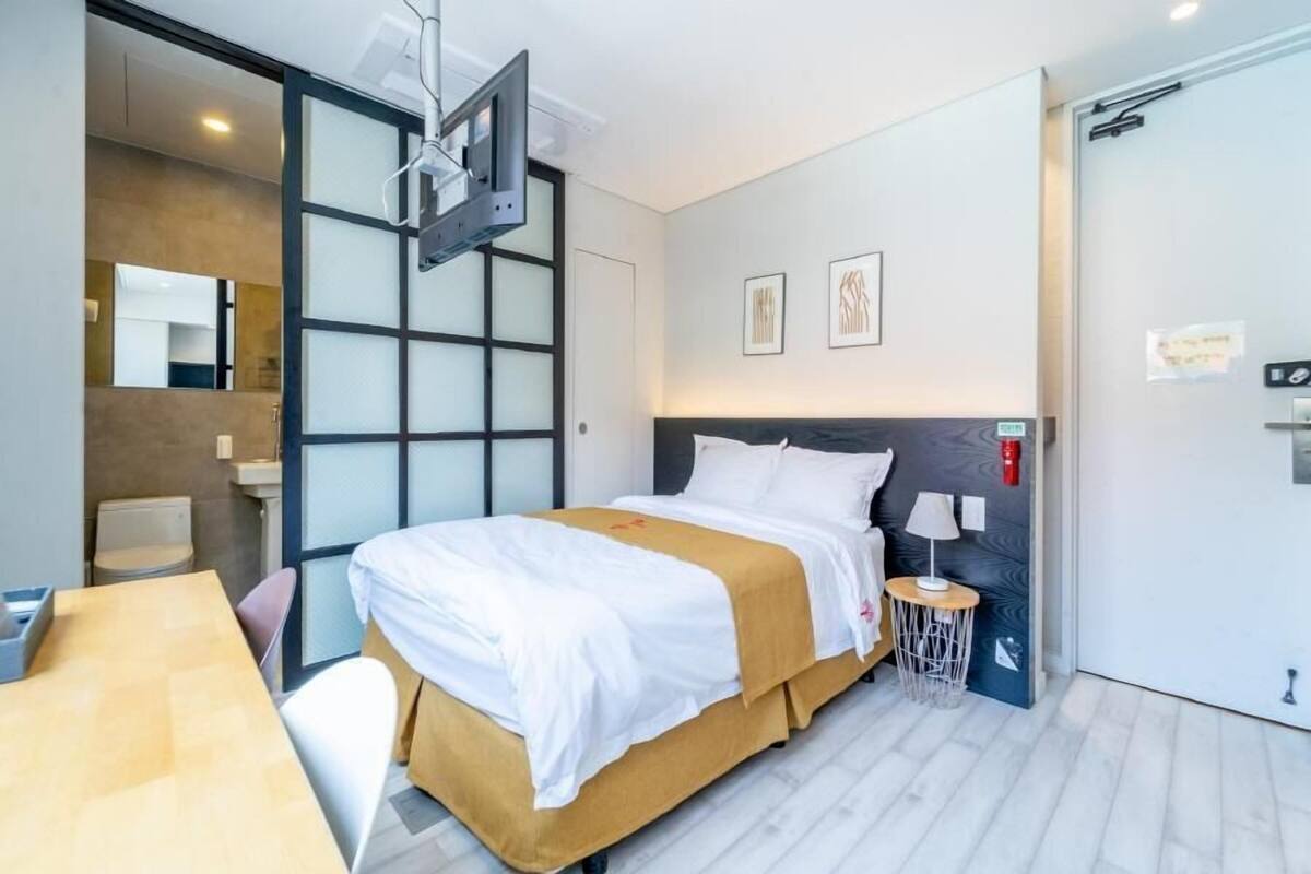 Habitació d'hotel moderna amb llit, escriptori, cadira, televisió penjada a la paret i una porta amb nassó.