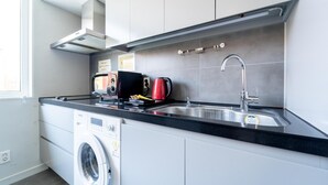 Una cocina moderna con lavadora integrada, microondas y hervidor sobre la encimera.