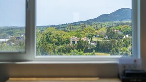Una habitación con un ventanal grande que da a un paisaje verde con casas y colinas.
