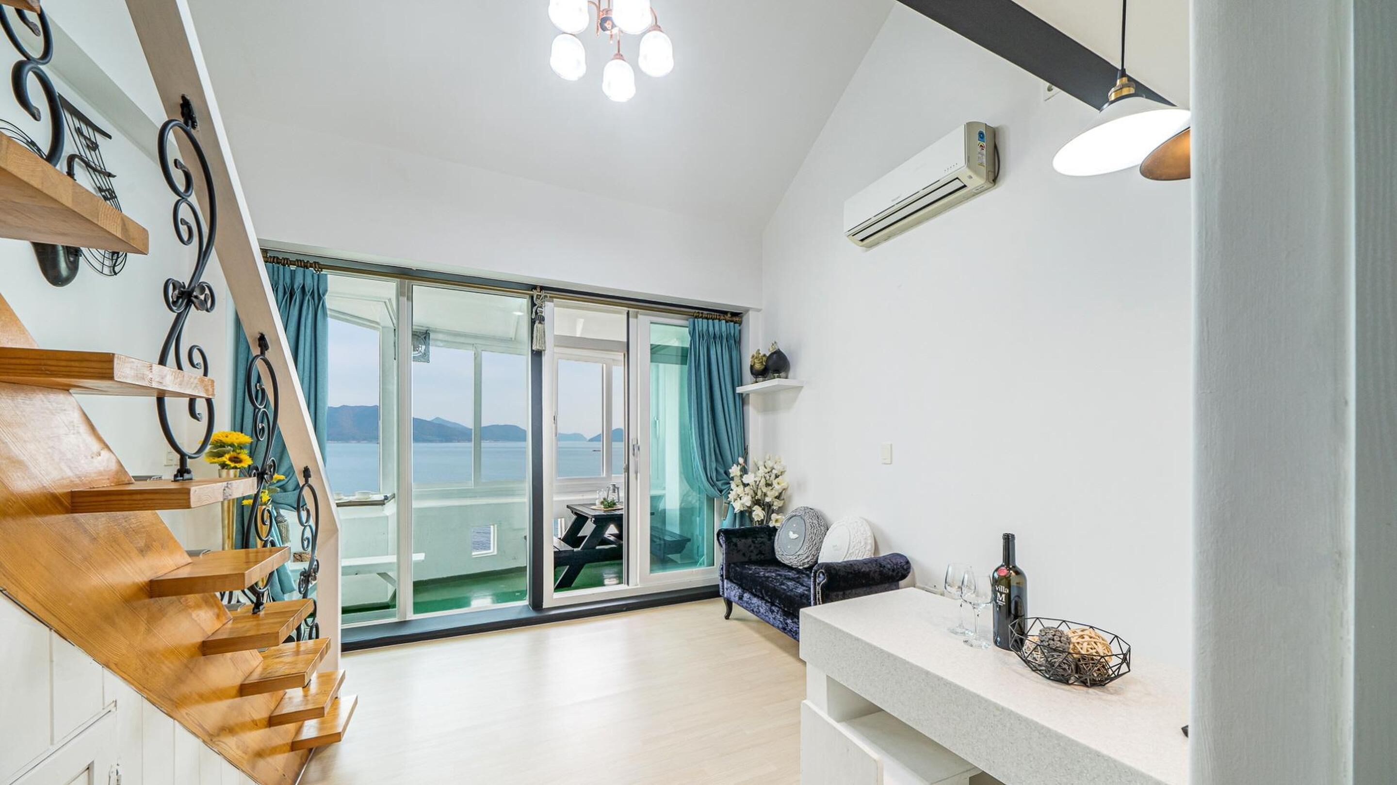 Uma sala de estar ampla com escada de madeira, varanda com vista para o mar e cozinha moderna.