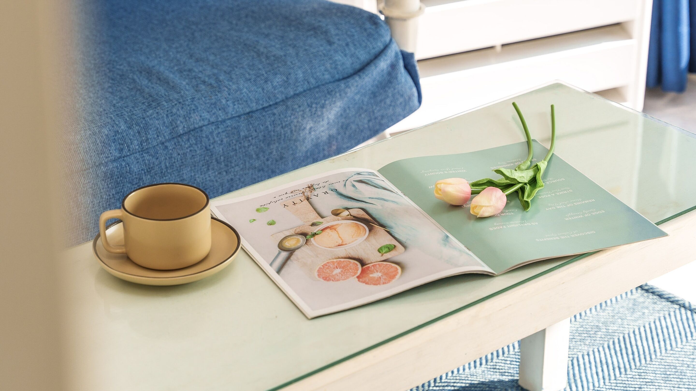 A magazine on a glass table with a cup and a pair of tulips.