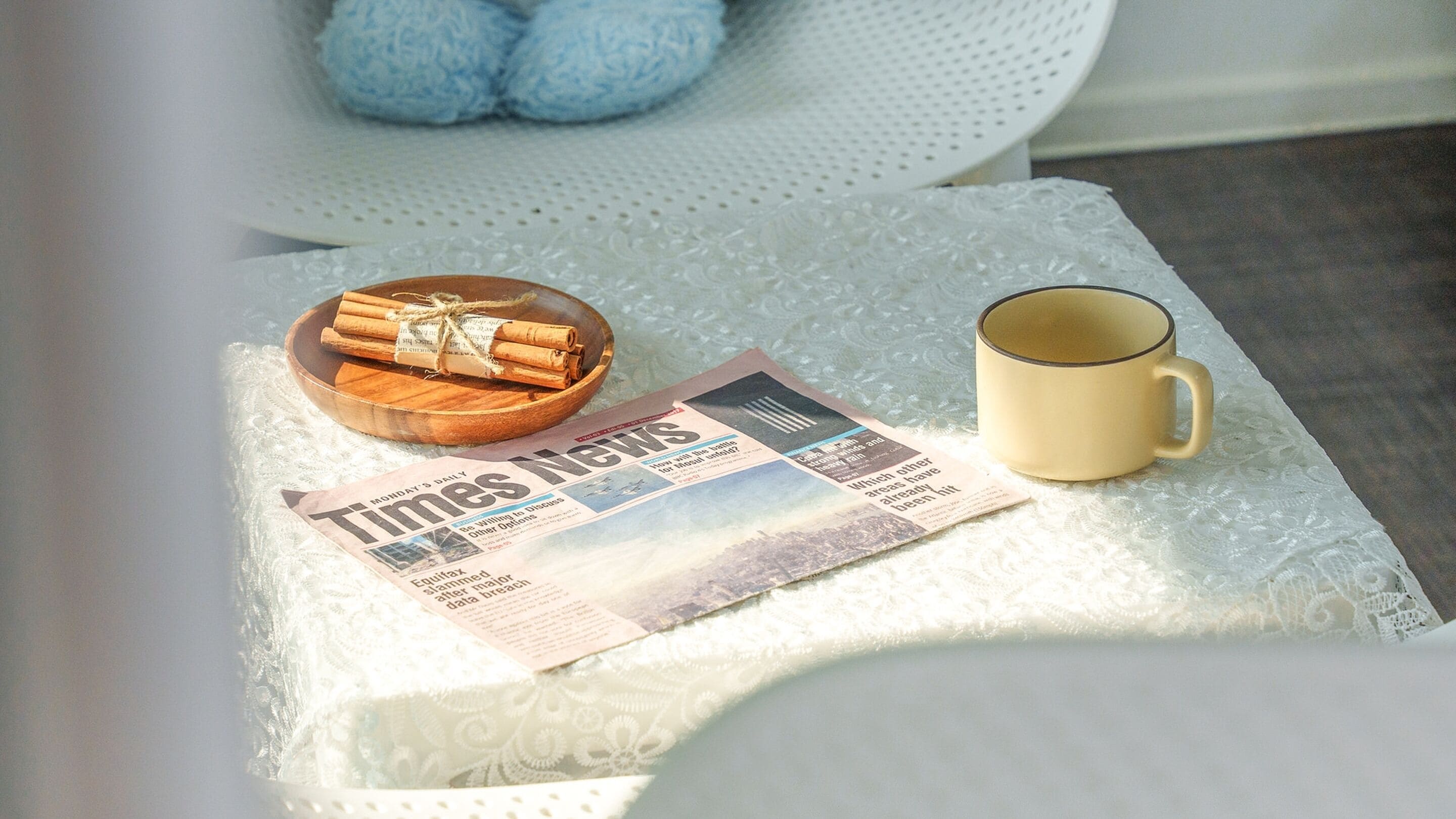 A newspaper, a mug, and a bowl of cinnamon rolls on a white table.