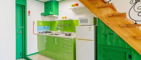 A compact kitchen with green cabinets, a white refrigerator, and a wooden staircase.