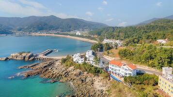 Un pueblo costero con un litoral rocoso, edificios a lo largo de la costa y montañas al fondo.