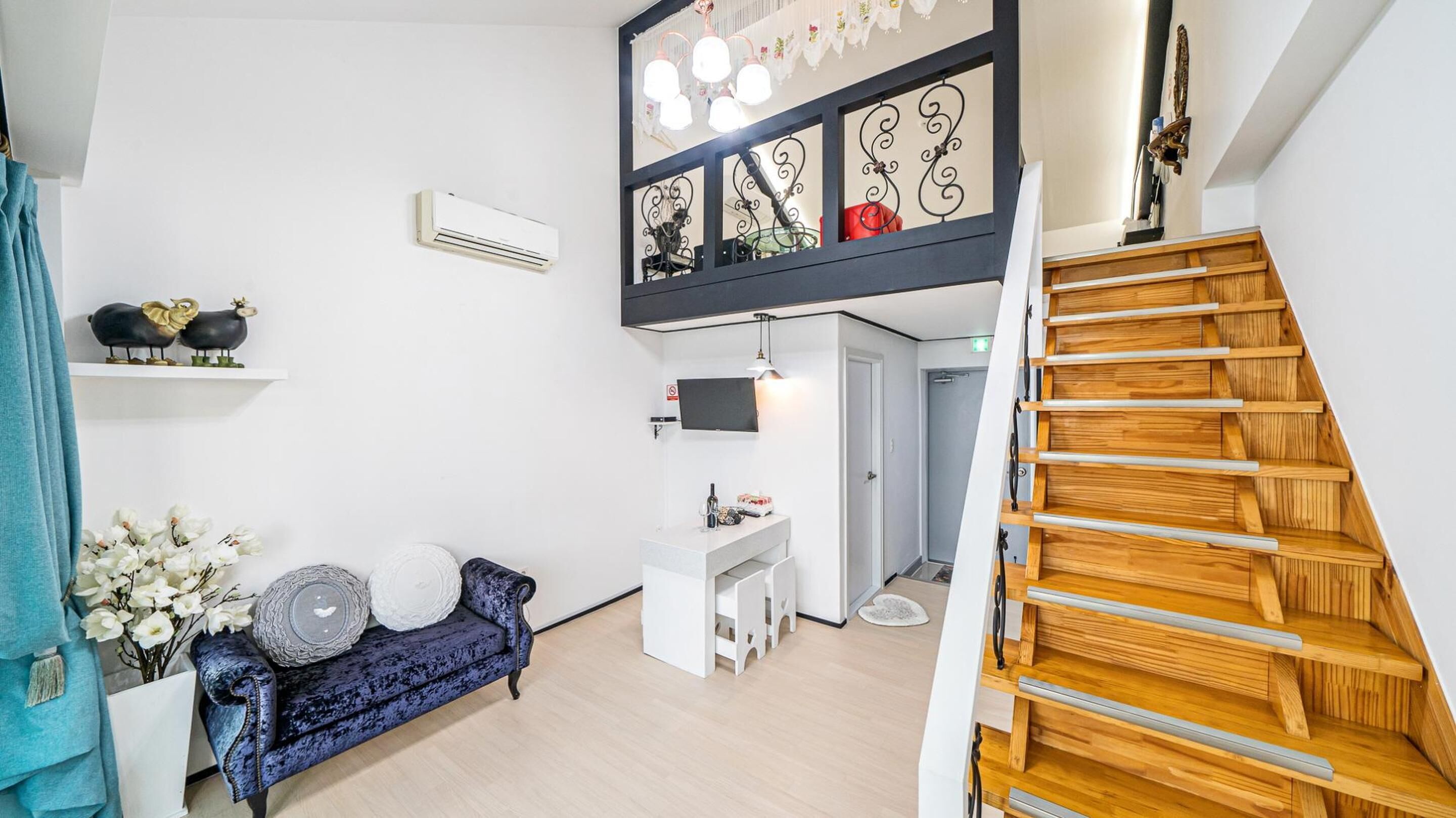 Una sala moderna con un sofá azul, una mesita blanca y una escalera con escalones de madera.