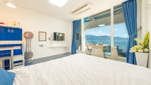 A hotel room with a bed, a TV, a window with a view of the sea, and a balcony with a table and chairs. - Namhae Opera House Pension (Namhae)