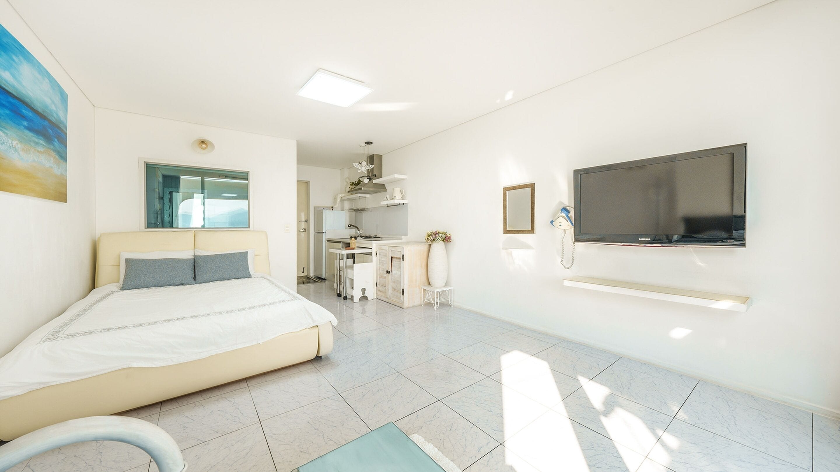 A modern hotel room with a bed, a TV, a desk, and a bathroom visible through an open door.