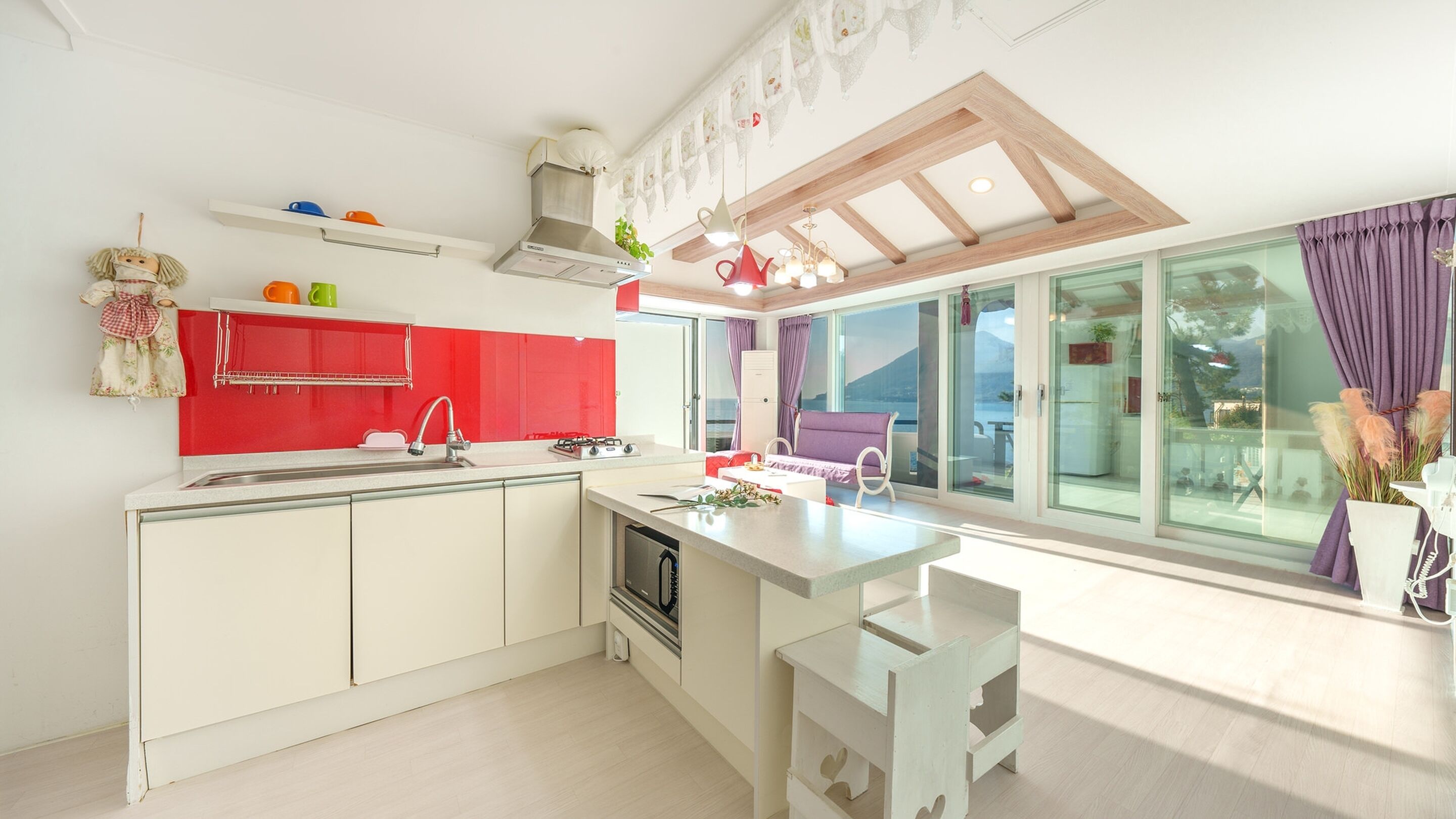 A modern kitchen with white cabinets, a red backsplash, and a large window overlooking a scenic view.