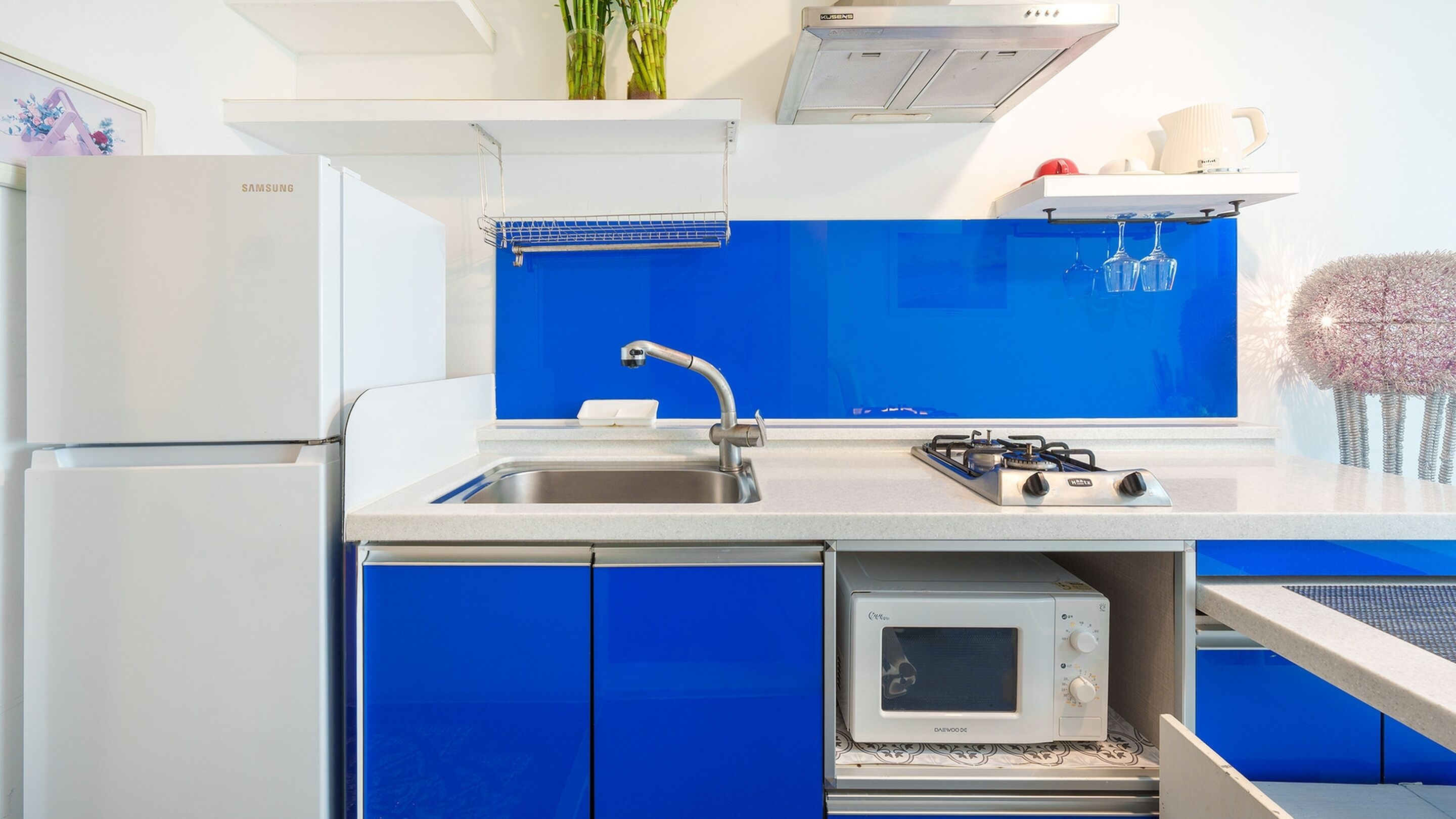 A modern kitchen with a white refrigerator, a blue backsplash, a stainless steel sink, a gas stove, and a microwave.