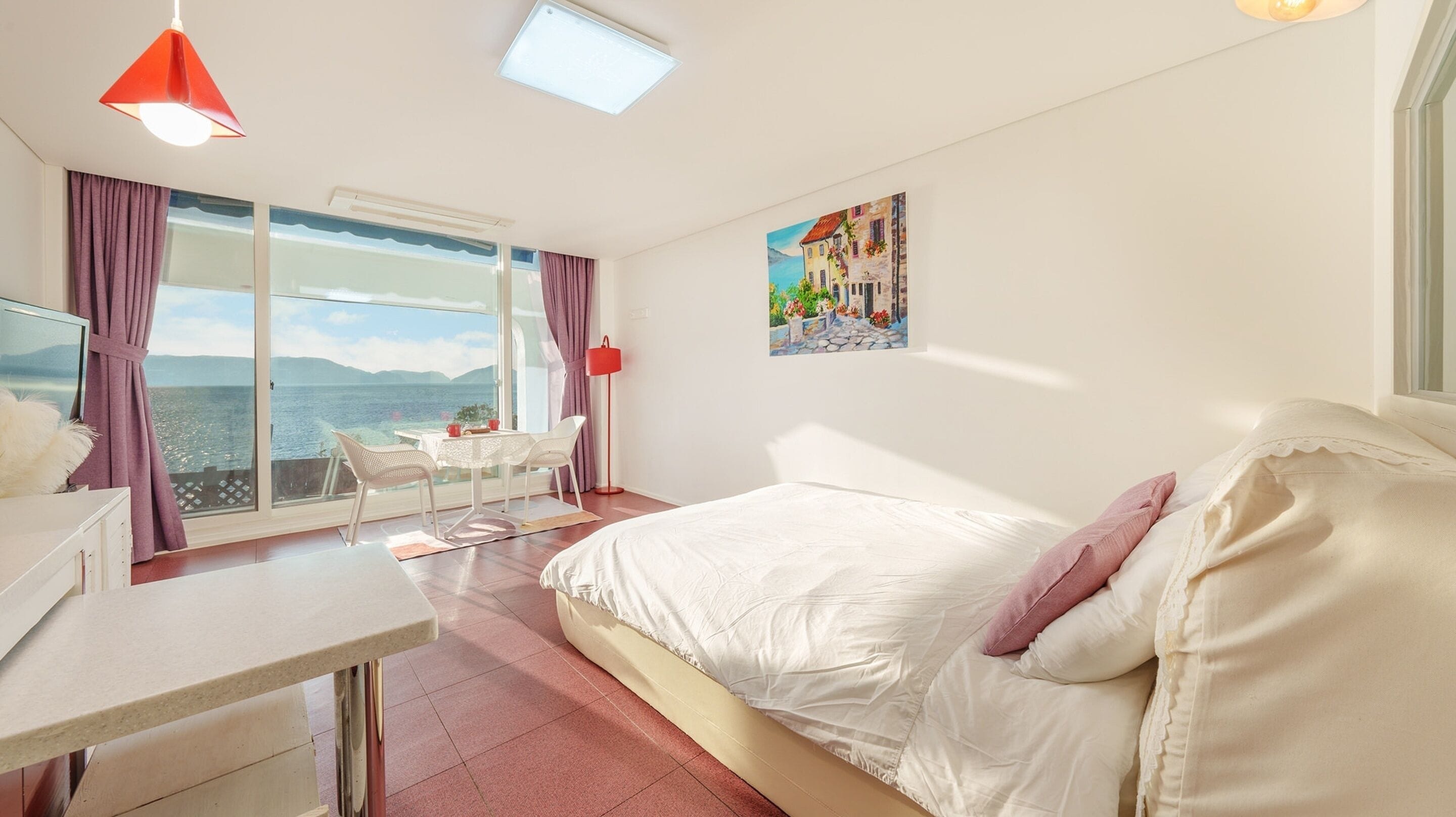 A bedroom with a large bed, a desk, a chair, and a window overlooking a body of water.