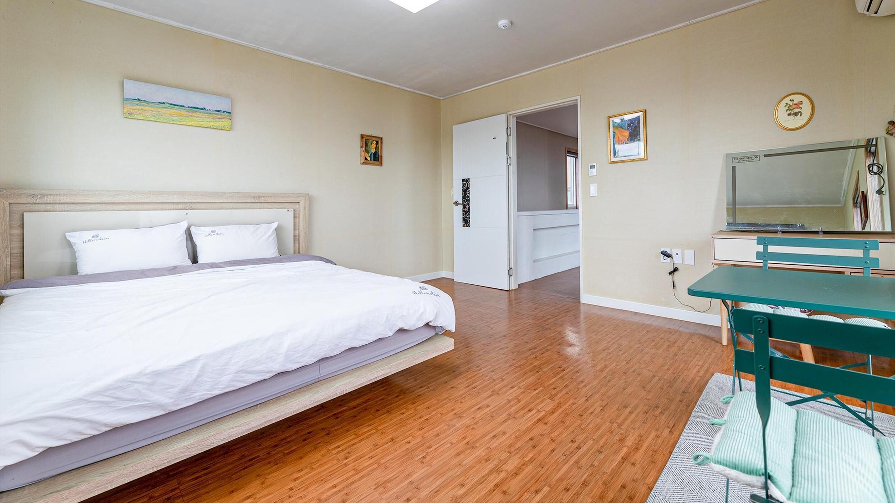 Un dormitorio con una cama, un escritorio y una silla. Hay una puerta que da a otra habitación.