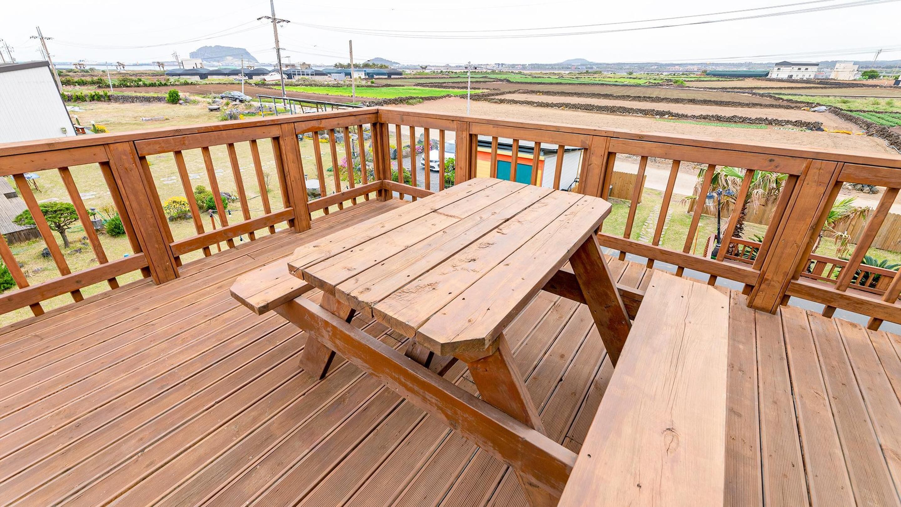 Eine Holzterrasse mit einem Picknicktisch und Blick auf Felder und Gebäude in der Ferne.