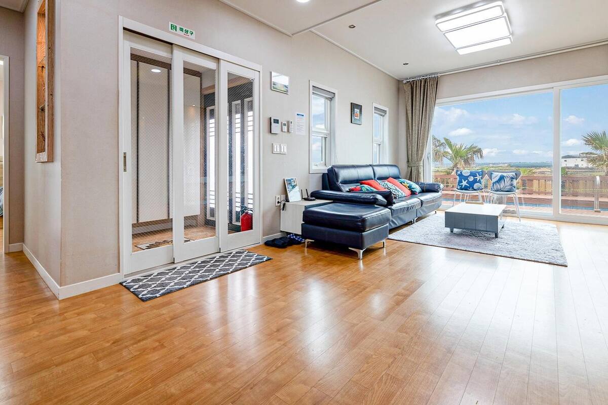 A spacious room with a large sliding glass door leading to a balcony, a black leather sofa, and a small table.