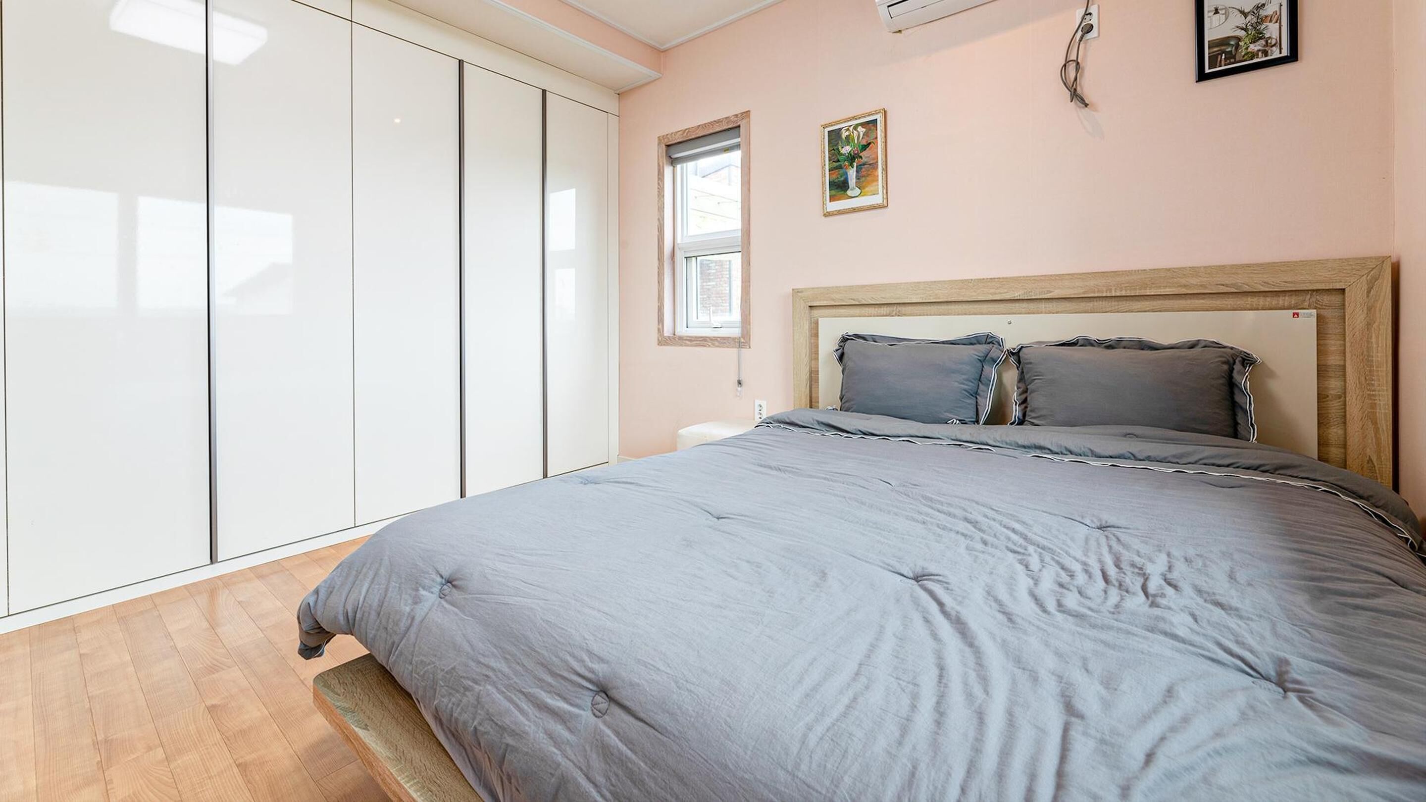 A bedroom with a bed, a wardrobe, a window, and a painting on the wall.